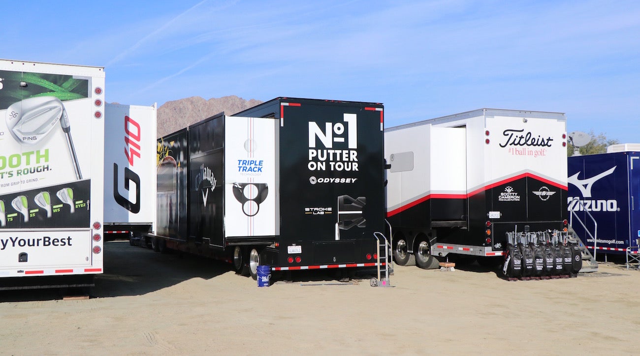 Tour trucks from different manufacturers set up in a parking lot near the putting green and driving range for quick access.