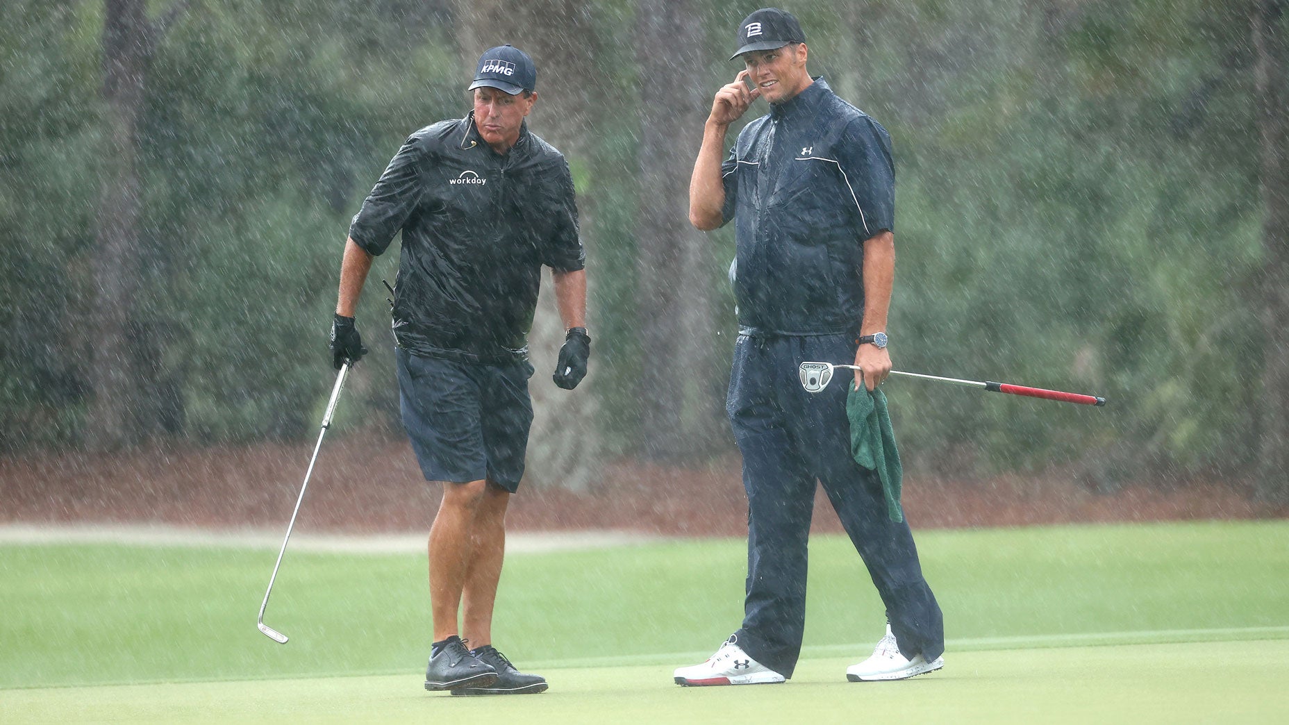 Phil Mickelson and Tom Brady stand in the rain on the 13th green at Medalist Golf Club.