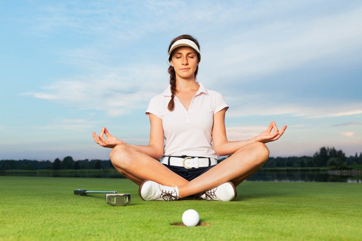 Girl golfer sitting in yoga posture on golf course meditating