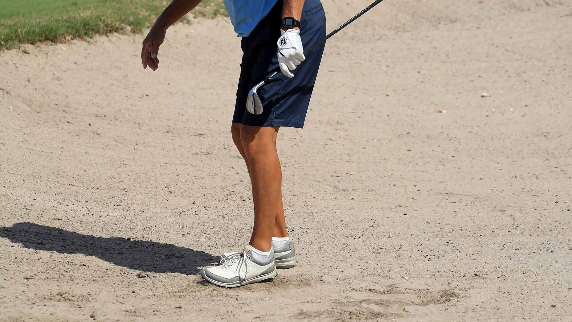 A man raking a bunker with his foot.