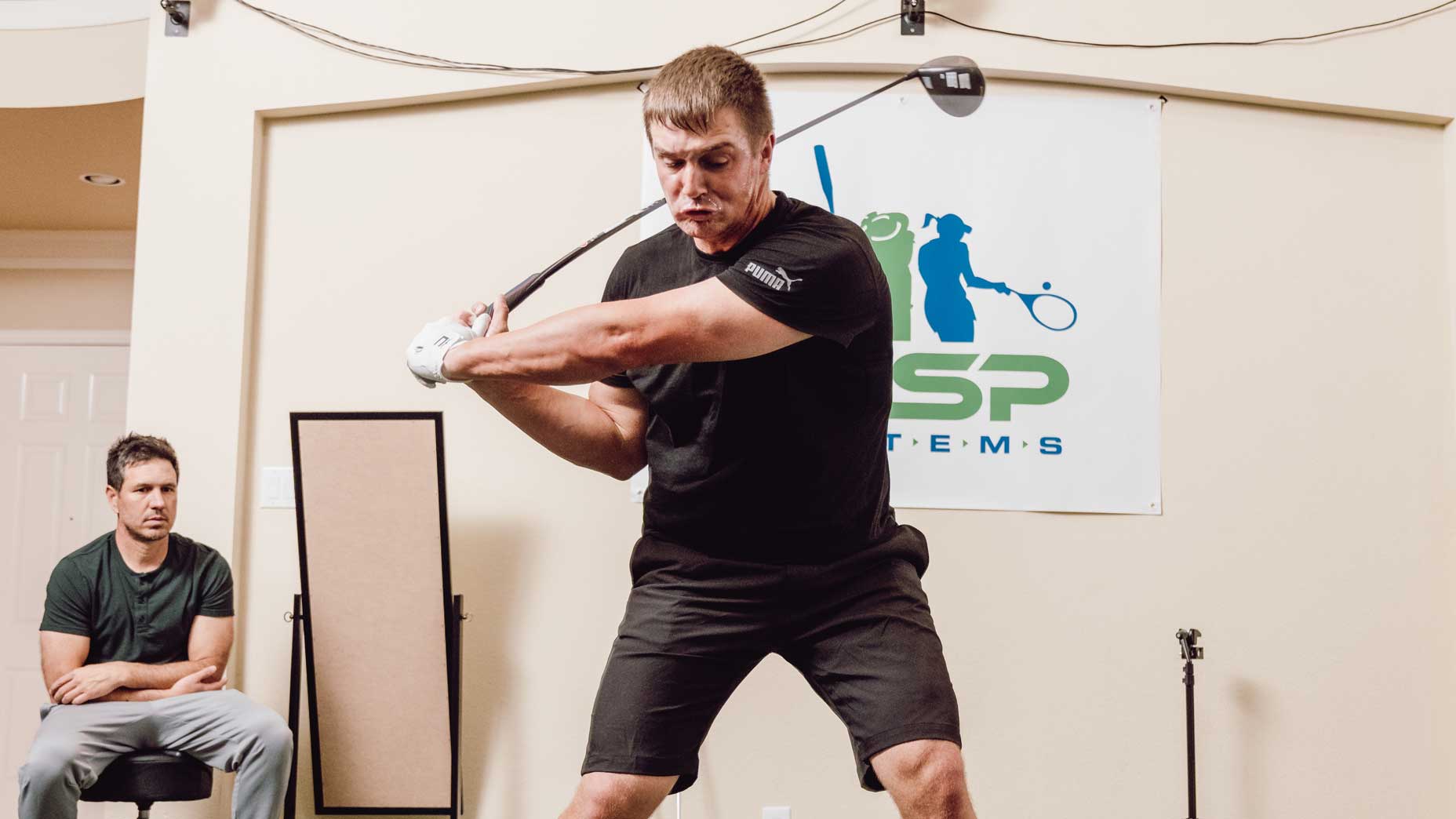 Byrson DeChambeau swings a golf training club indoors