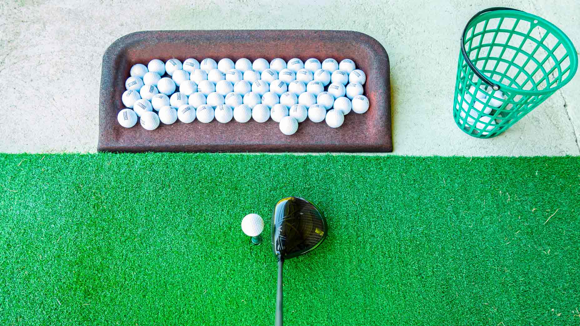 golf driver rests on driving range with practice golf ballsmat