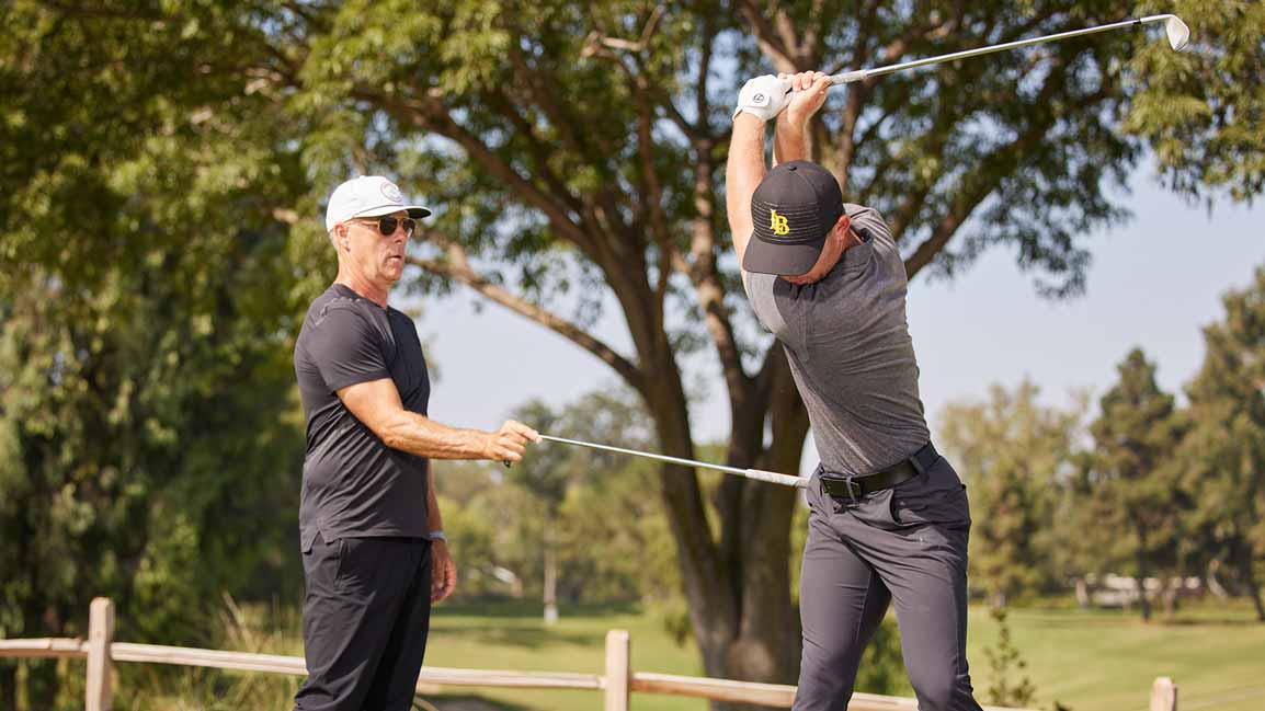 man pushes golfers hip with shaft