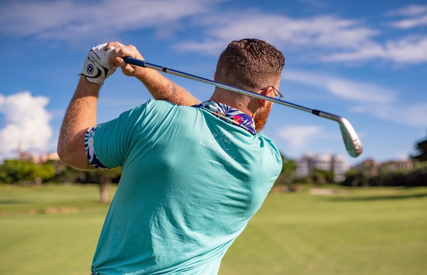 Man swinging a golf club in a teal shirt