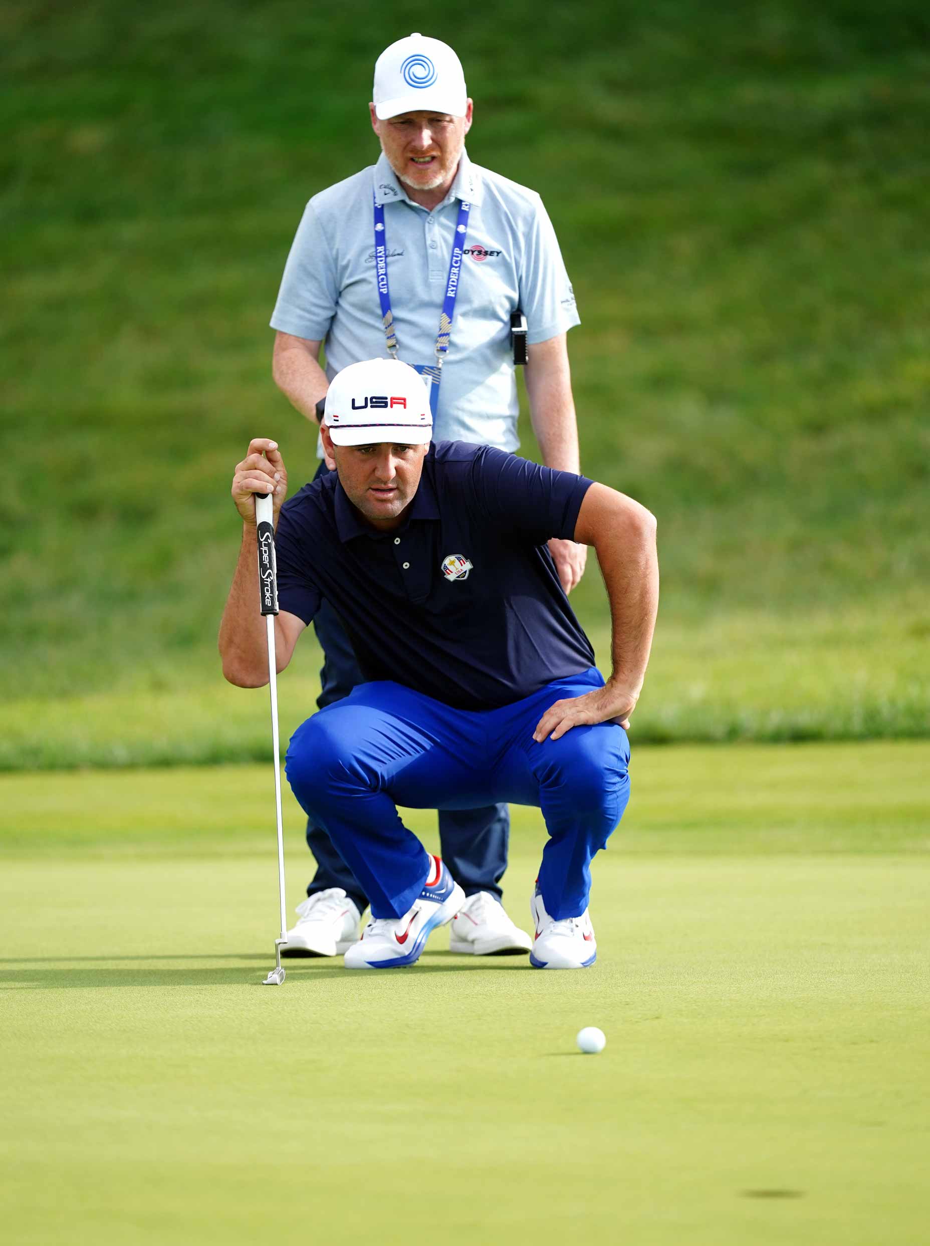 Scottie Scheffler on the practice green with Phil Kenyon looking on.