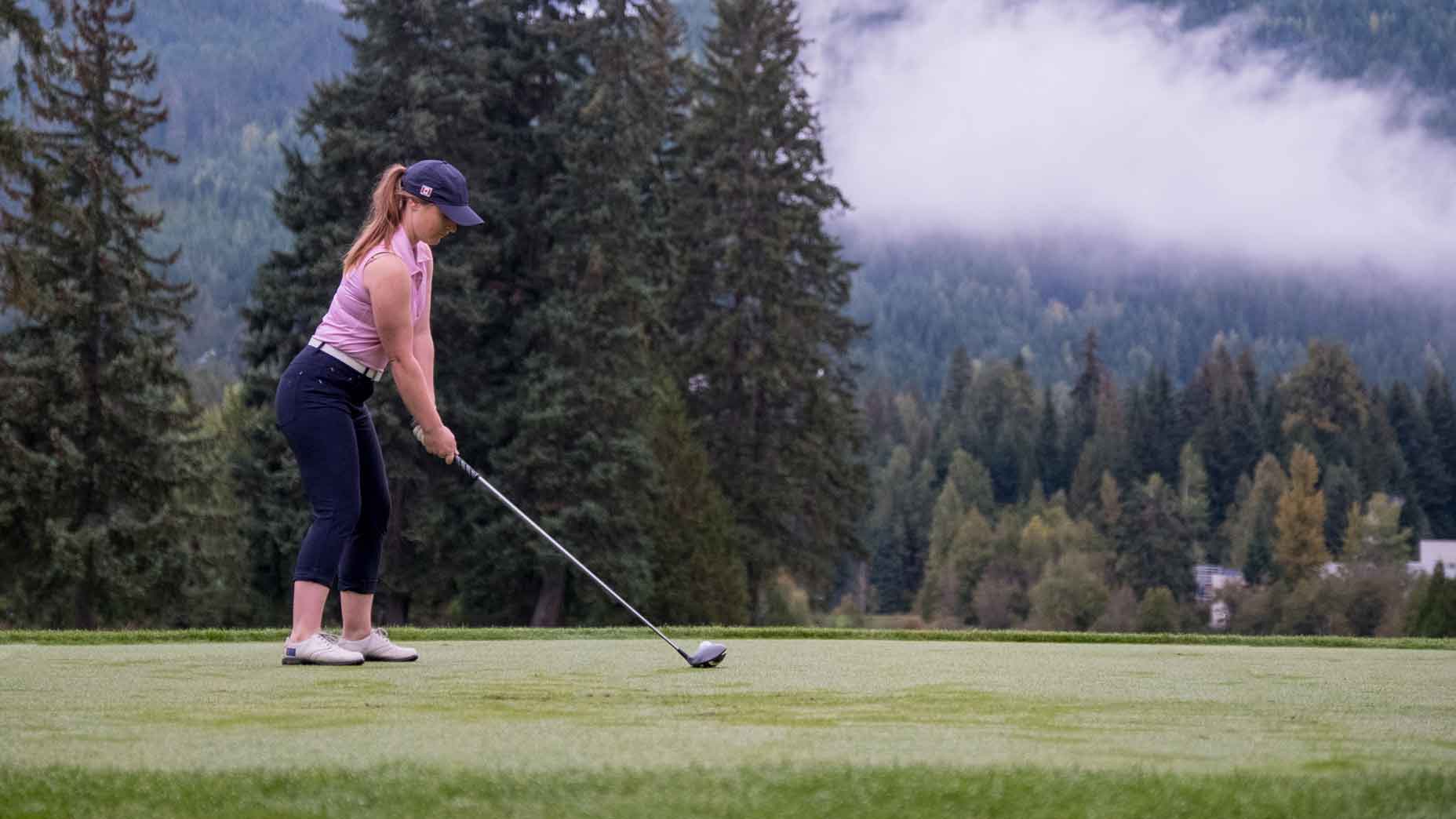 Young woman playing golf on field. Full length length image of a female golf player wearing sports clothing. Golfer hitting her shot to a green.
