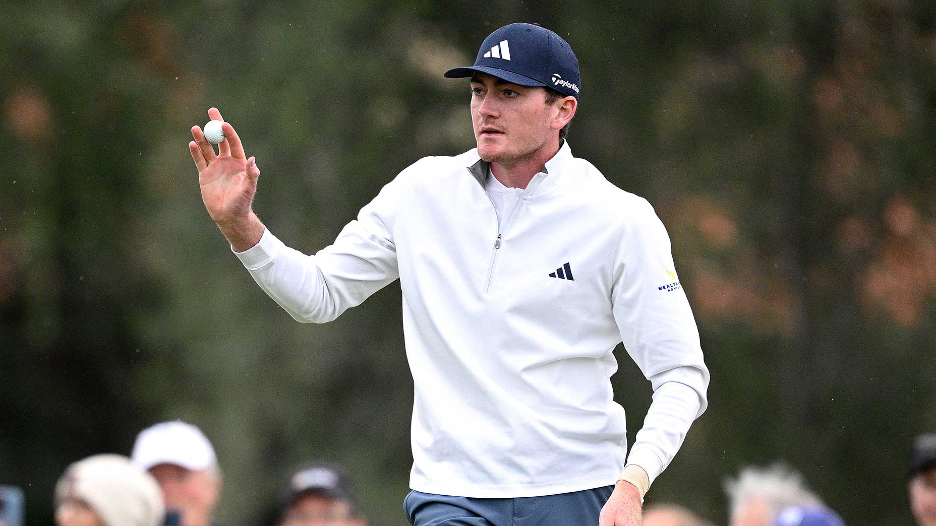 nick dunlap waves to fans in white shirt and blue hat at the American Express