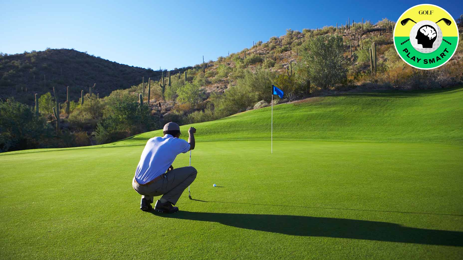 a golfer in a blue shirt crouches down to read a putt on a green