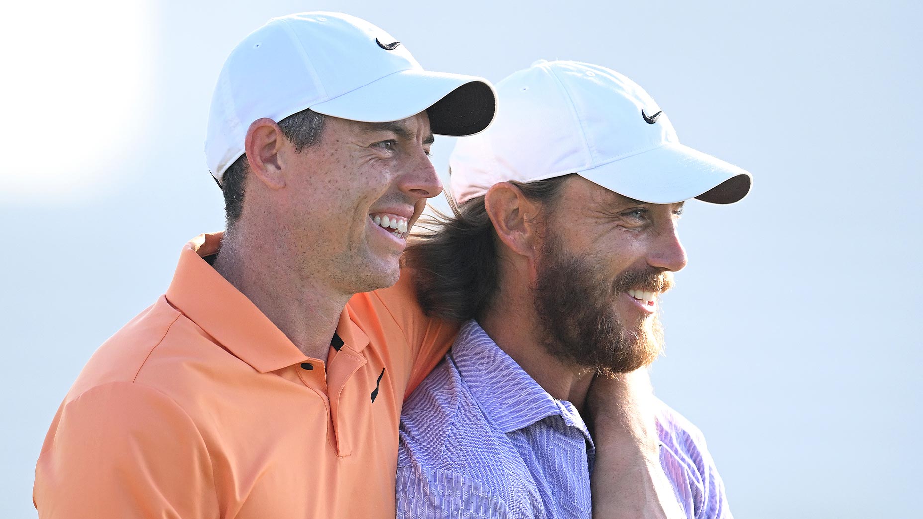 Rory McIlroy in orange shirt wraps arm around Tommy Fleetwood in purple shirt at Dubai Invitational