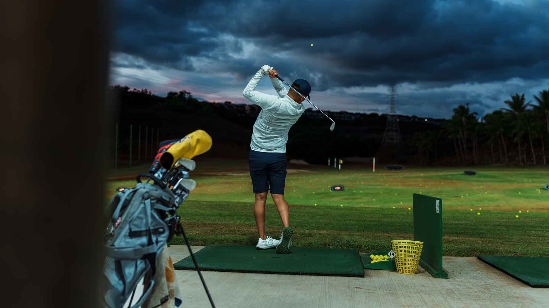 golfer hits balls on driving range at night
