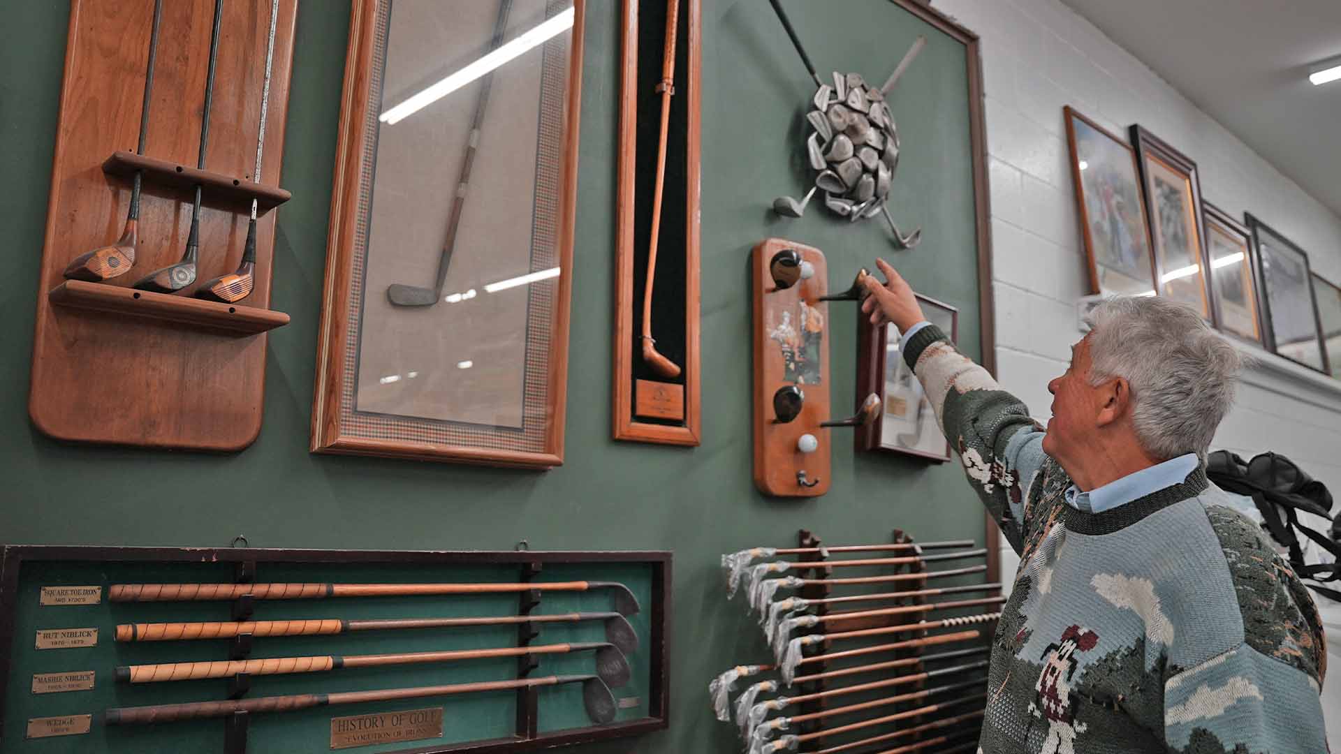 Robert Zokoe pointing at his collection of old golf club displays.