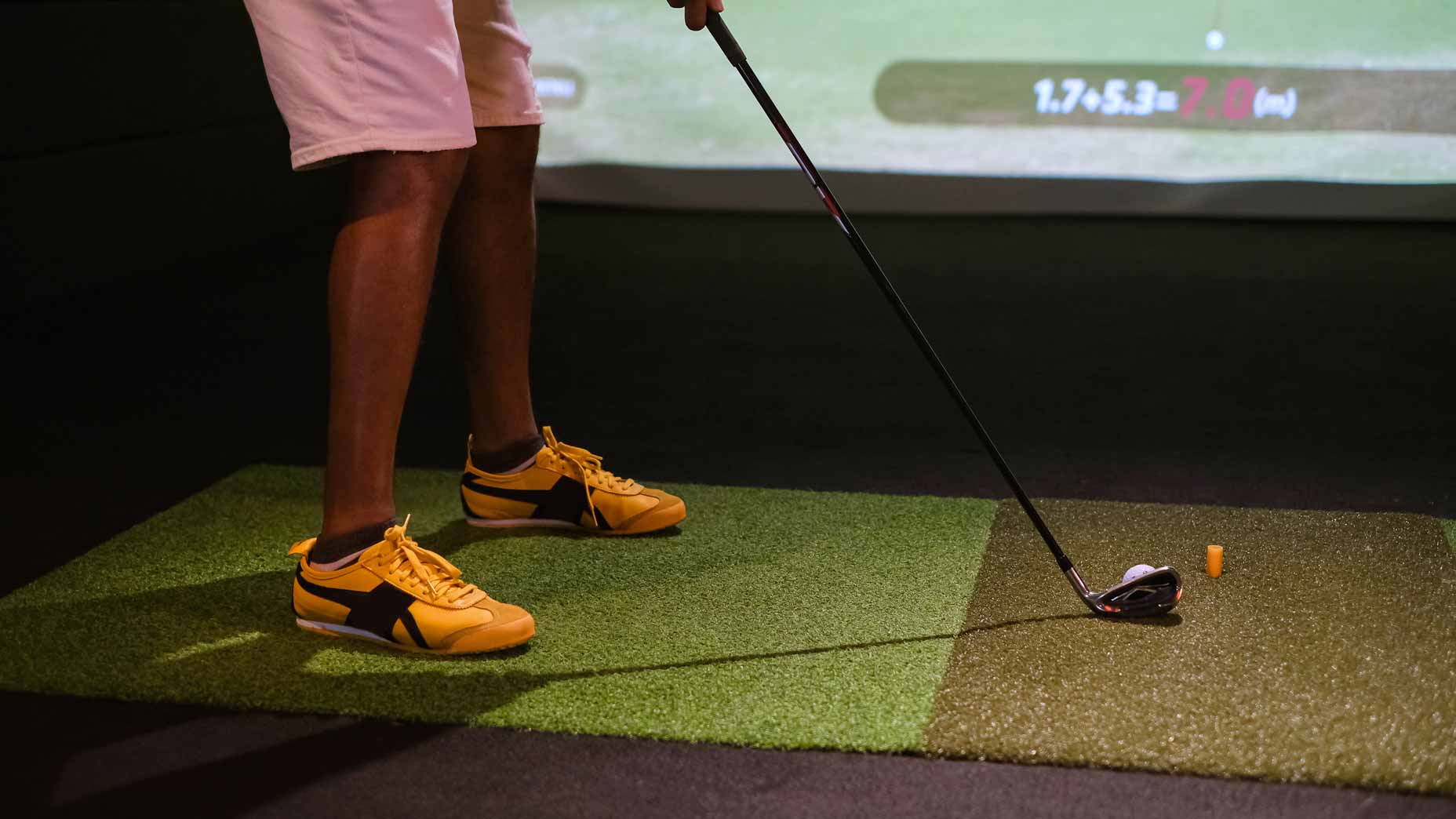 golfer in yellow shoes hits ball on simulator