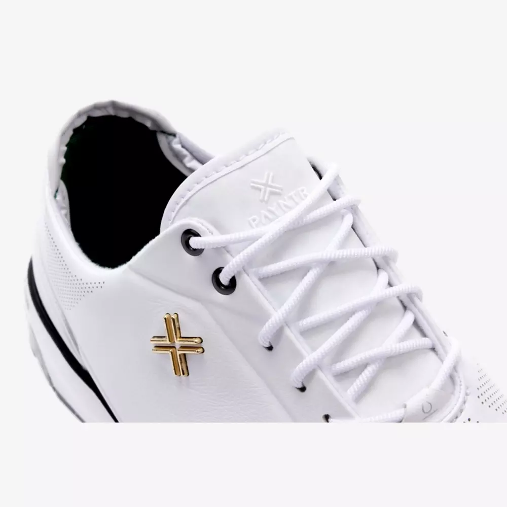 A close-up of a white sneaker with white laces, black accents, and a small gold cross-shaped logo on the side. Reminiscent of the best Jordan golf shoes, the brand name BANTU is embossed on the tongue.