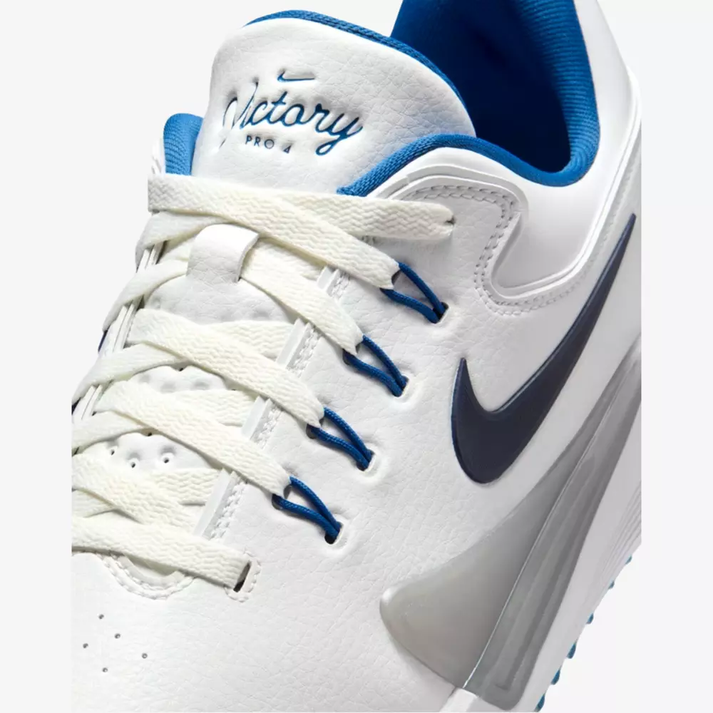 Close-up of a white Nike athletic shoe with blue accents, ideal for those seeking the best golf shoes 2026. The tongue reads Victory Pro in blue, and a large black Nike swoosh appears on the side. White laces and blue inner lining complete the look.