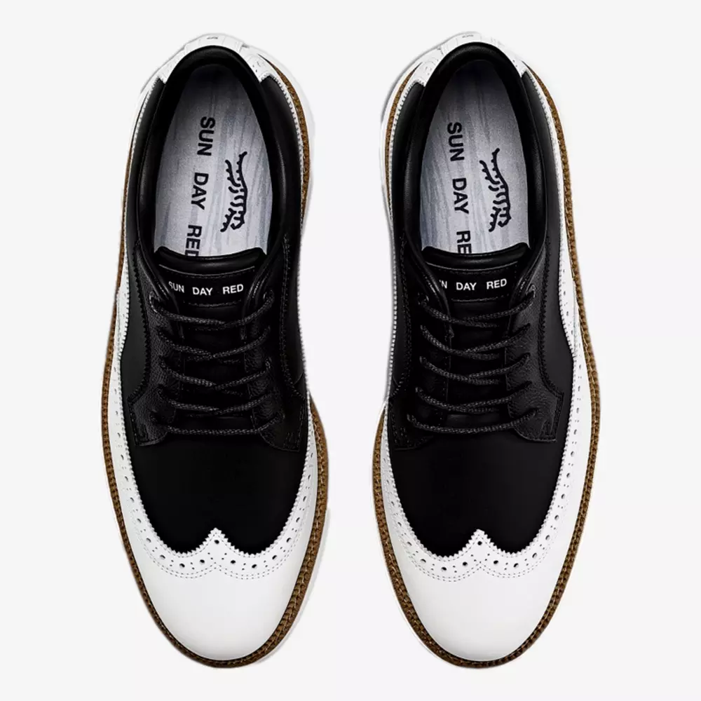 A pair of black and white wingtip shoes with brown soles, viewed from above. The insoles display the text SUN DAY RED. These elegant shoes, styled like the best Jordan golf shoes, feature black laces and decorative perforations on the toe caps.