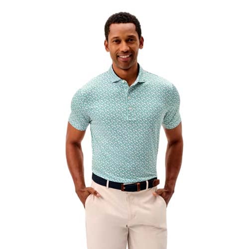 A man stands smiling with his hands in his pockets, wearing a teal short-sleeve patterned polo shirt and beige pants—one of the best looks from The First Major—against a plain white background.