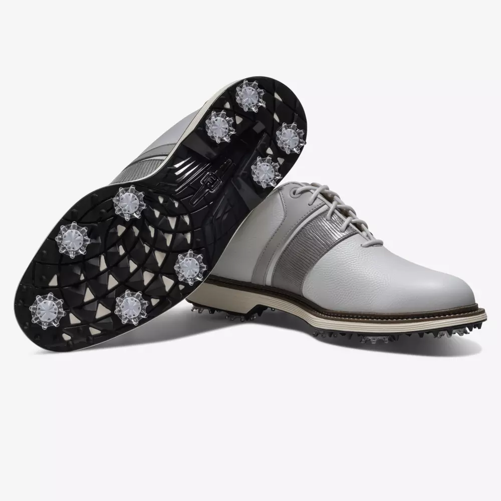 A pair of white golf shoes with black and gray accents, inspired by the best Jordan golf shoes, feature textured soles and multiple soft spikes for traction. One shoe stands upright while the other displays its spiked sole.
