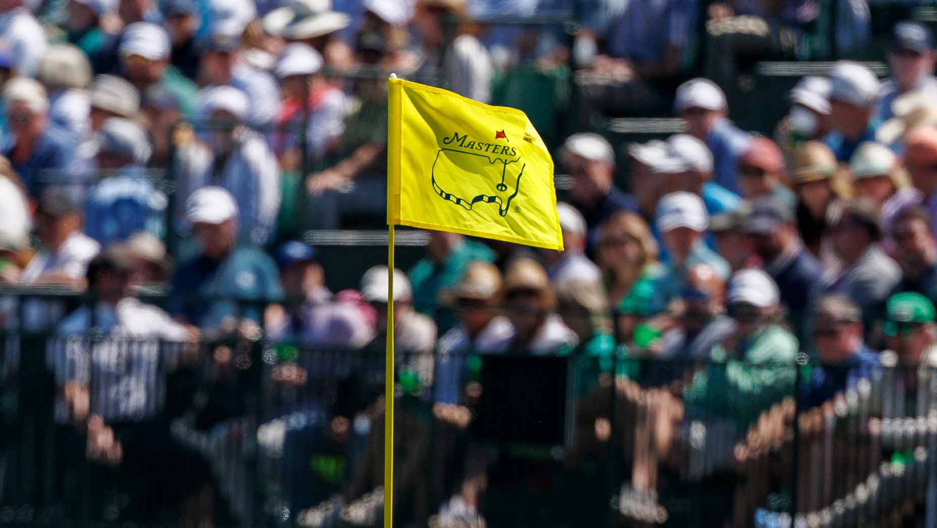 2026 Masters Saturday tee times: Yellow flag at Augusta National with fans in background.