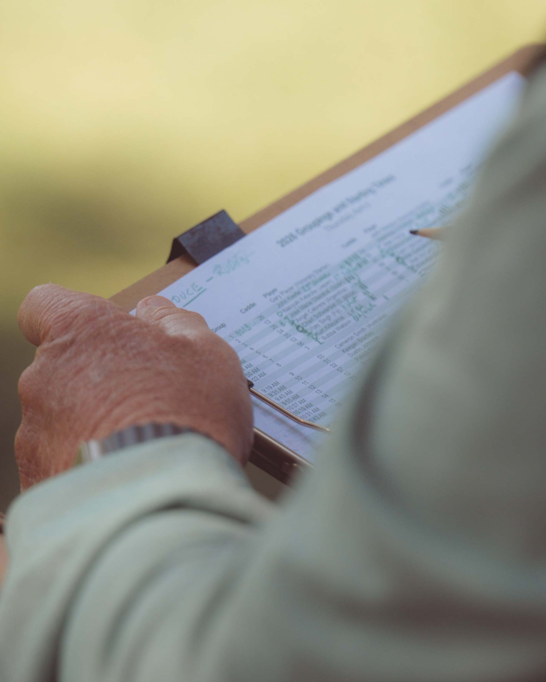 A person holding a clipboard with a printed form attached, appearing to review or fill out information—perhaps recording scores for a walk all 18 at Augusta National. The focus is on the hands and clipboard, with the background blurred.