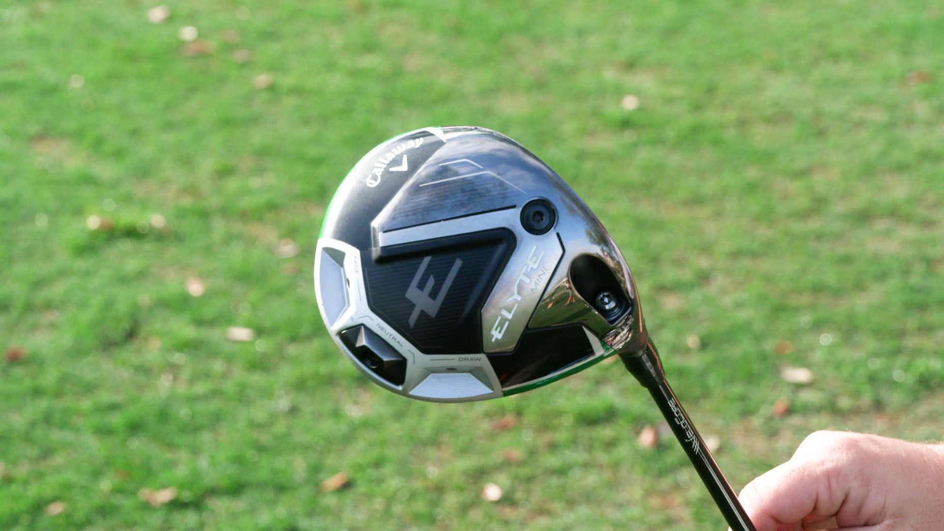 A person holds a modern golf driver with a metallic and black head labeled ELVT against a background of green grass.