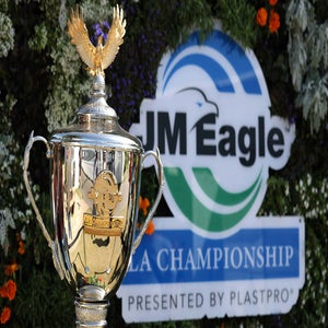 A silver trophy with an eagle figure on top stands in front of a JM Eagle LA Championship sign, surrounded by greenery and flowers, highlighting the LPGA purse increase at one of the season's richest tournaments.