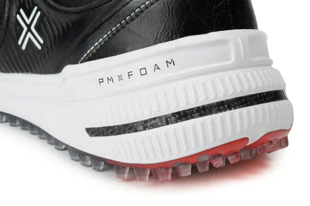 Close-up of the heel of a black and white sneaker, one of the best golf shoes 2026, with PM FOAM text on the white midsole and red-tipped rubber cleats on the outsole. The upper features a white stitched X logo.