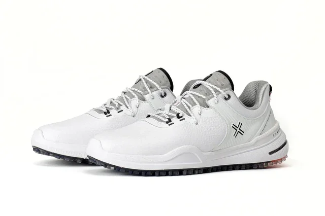 A pair of white athletic sneakers with gray accents, black treaded soles, and a black geometric logo on the side—styled to rival the best golf shoes 2026—displayed against a plain white background.
