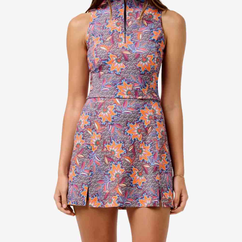 A woman wearing a sleeveless, high-neck, floral dress with a colorful pattern in purple, orange, and pink—a stylish choice for Mother’s Day. The dress features a fitted waist and short hemline with small front slits.