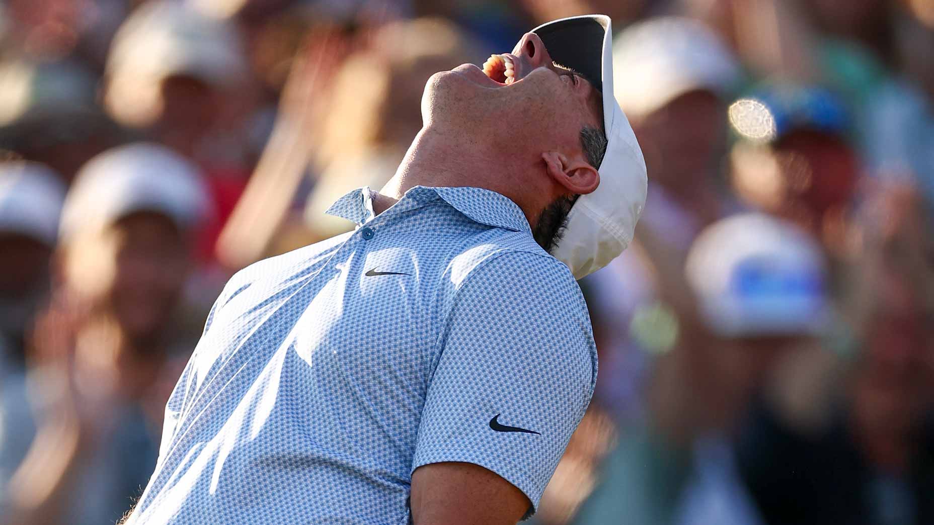A golfer wearing a white cap and light blue patterned shirt leans back, mouth open in celebration or relief at Augusta, with a blurred crowd cheering in the background&mdash;capturing the electric atmosphere of the Masters.