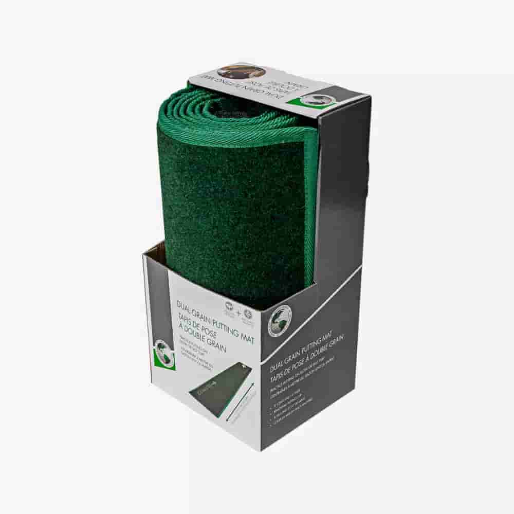 A rolled-up green dual grain putting mat displayed upright in its original black and white packaging, with part of the mat visible and product details printed on the box—an ideal companion for those seeking the best golf bags 2026.