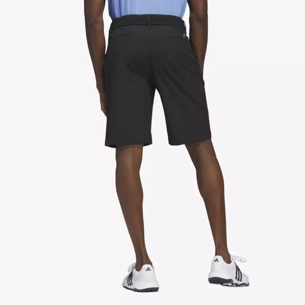 A person wearing black shorts, a black belt, white athletic shoes, and a light blue shirt stands facing away from the camera against a plain background—perhaps ready to pack one of the best golf travel bags for their next adventure.