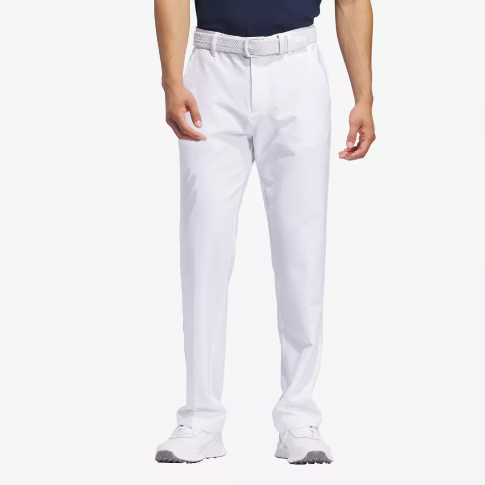 A man wearing white golf pants, a white belt, white golf shoes, and a dark shirt stands with his hands relaxed by his sides against a plain white background—ready for the fairway or packing the best golf travel bags for his next trip.