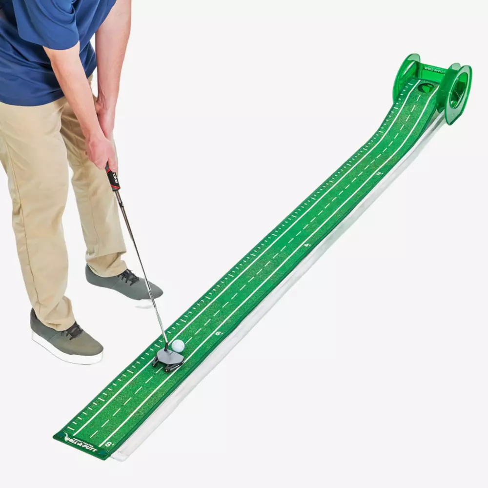 Person in khaki pants and gray shoes using a golf putter to hit a ball on a long, green indoor putting mat with white markings and a raised ball return system—one of the best deals under $50.