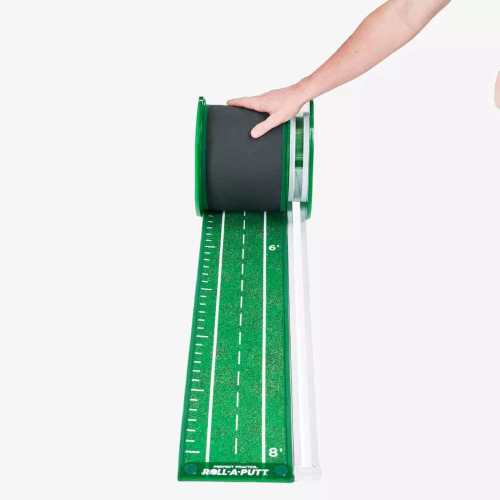 A person’s hand unrolls a green putting mat with white distance markings and a simulated turf surface, resembling a miniature golf fairway, onto a white floor—one of the best deals under $50.