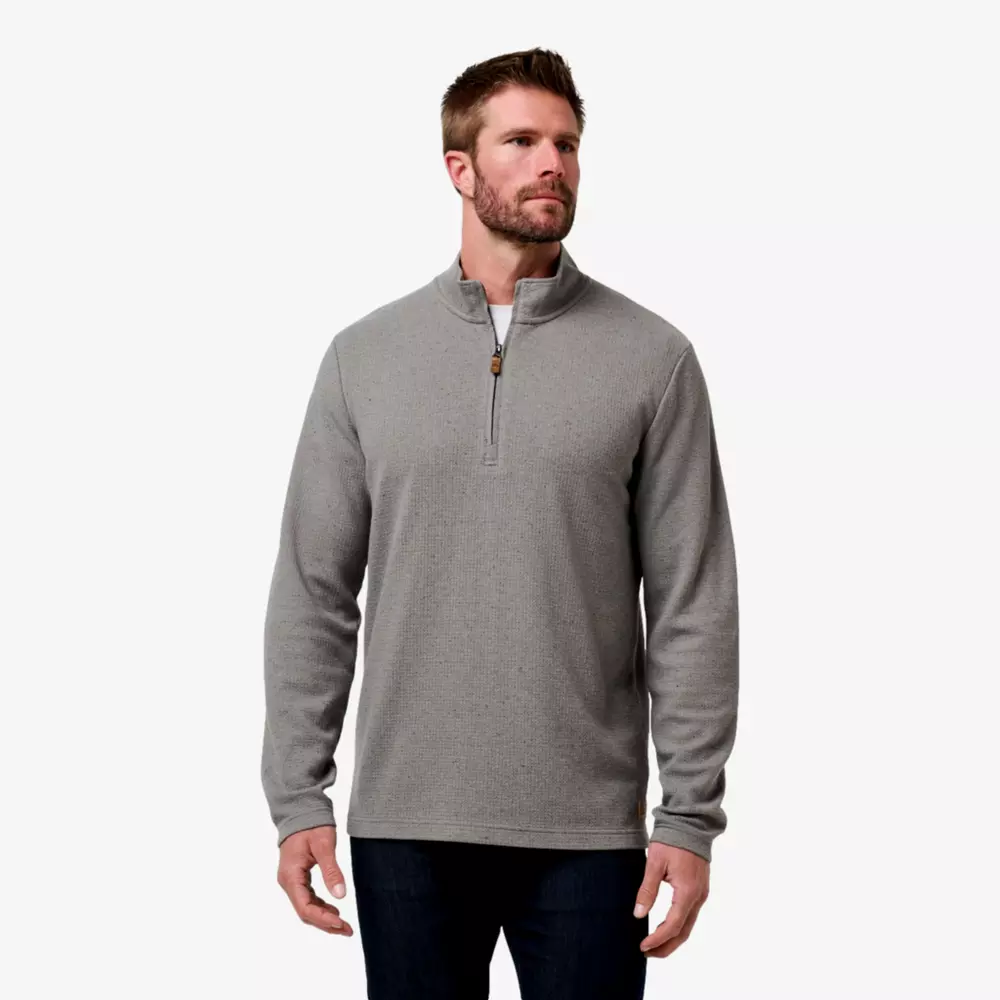 A man wearing a light gray quarter-zip pullover sweater and dark jeans—one of the best deals under $50—stands against a plain white background, looking slightly to the side with his hands relaxed at his sides.