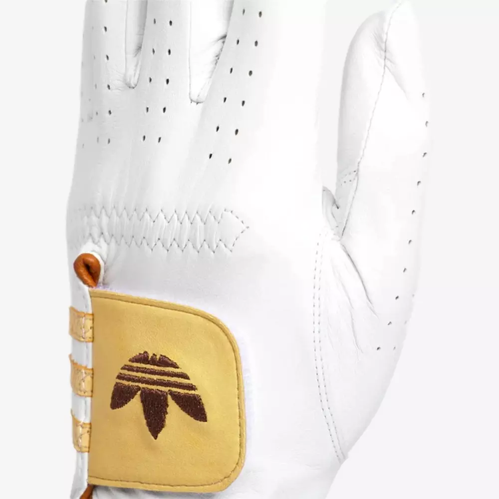 A white leather glove with small ventilation holes and a tan patch featuring a brown stitched logo on the wrist. Three gold-colored fasteners are visible on the side of the patch—a stylish match for those searching for the best golf bags 2026.