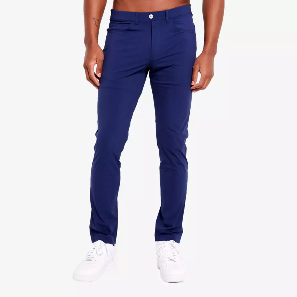 A person wearing fitted, navy blue pants—perfect for pairing with the best golf travel bags—and white sneakers stands against a plain, light background. The pants feature a button and zipper closure, with arms relaxed by their sides.
