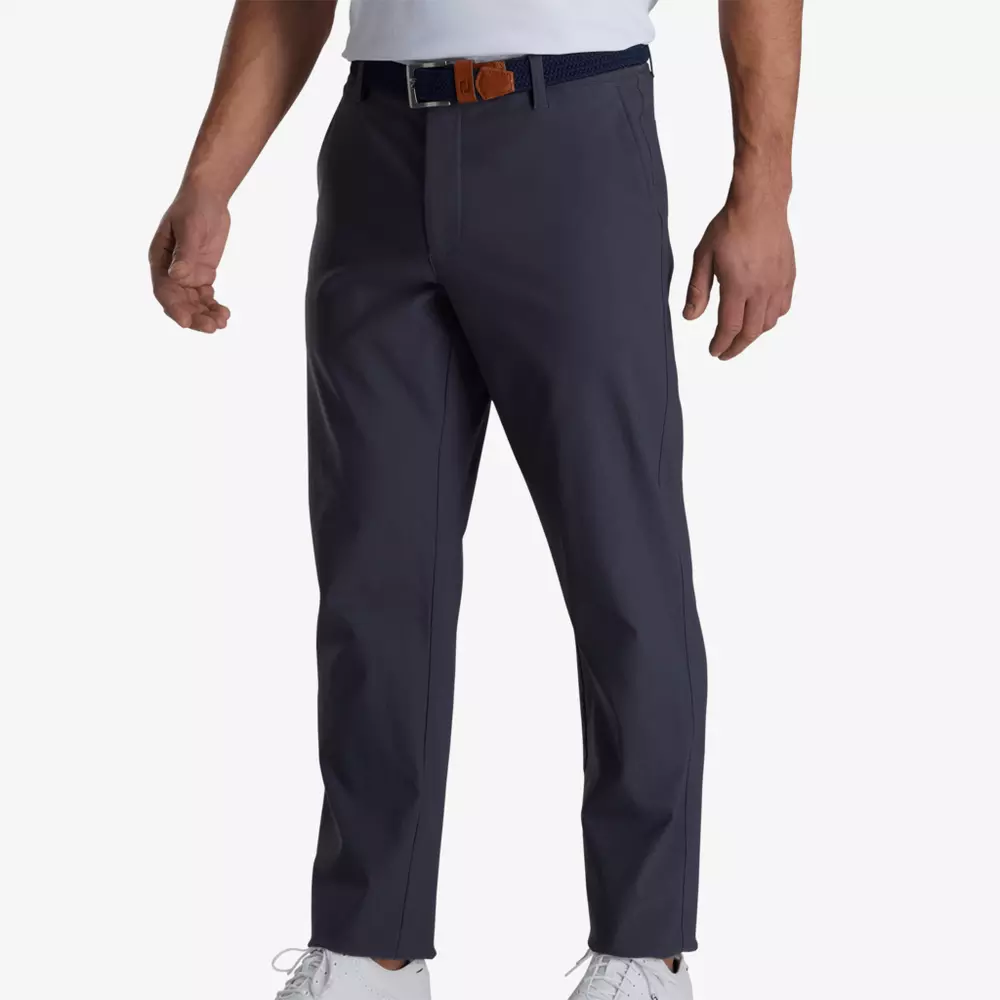 A person wearing navy blue pants with a black belt, a white shirt tucked in, and white sneakers stands against a plain white background, ready to explore with the confidence of someone carrying the best golf travel bags.
