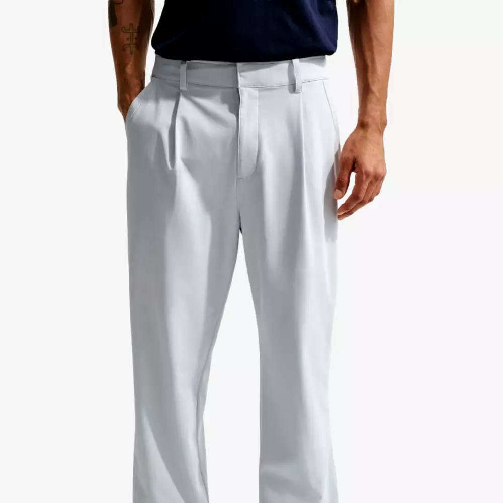 A person wearing light gray pleated dress pants with belt loops and a dark navy shirt, shown from waist to mid-thigh, standing casually as if ready to pack for a trip with one of the best golf travel bags.