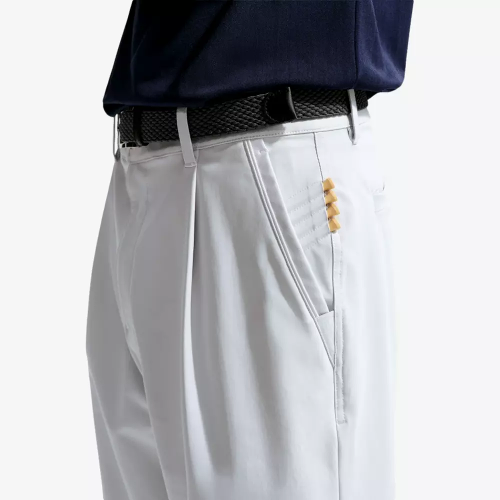 A person wearing white pants with a black belt and a navy shirt, likely ready for the course. Five small tees peek from a right pocket—perfect for those packing the best golf travel bags. Only the lower torso is visible.