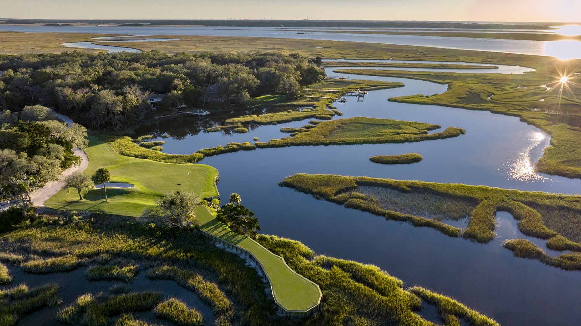 Aerial view of Omni Amelia Island Resort’s lush golf course, perfect for a buddies' trip getaway, surrounded by winding water channels, marshland, and greenery with sunlight reflecting off the water and a distant treeline.