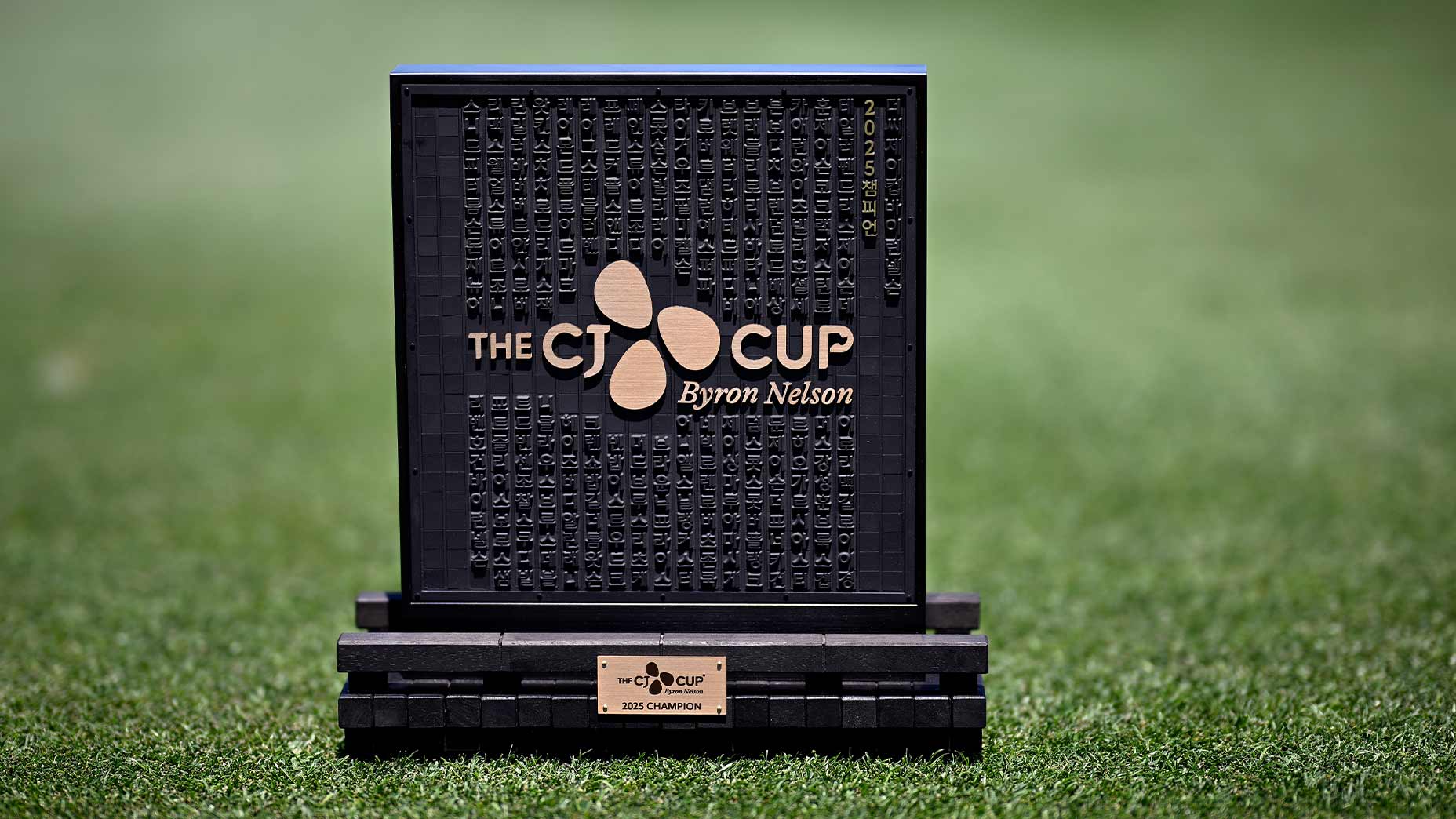A black and gold square trophy with The CJ CUP Byron Nelson text, raised letters, and a plaque reading 2023 Champion, symbolizes victory and the impressive CJ CUP Byron Nelson purse, displayed on green grass.
