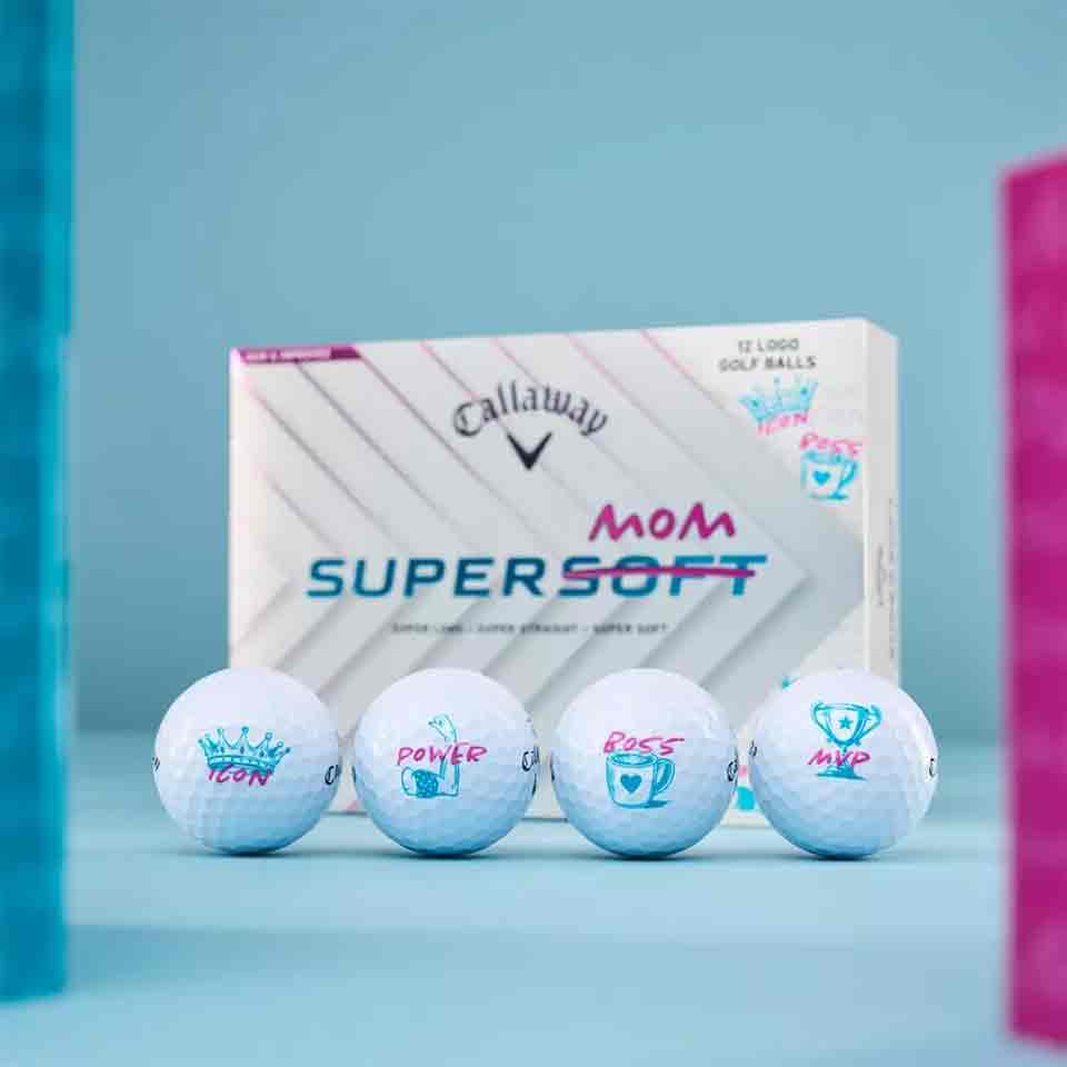 Four Callaway golf balls with hand-drawn designs and words like ICON, POWER, BOSS, and MVP are lined up in front of a Callaway Supersoft Mom box—perfect as stylish accessories or unique Mother’s Day gifts. Pink and blue objects frame the image.