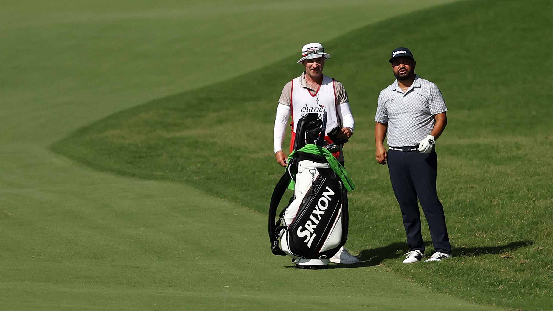 A golfer and his caddie stand on a sunlit fairway, surrounded by green grass, both gazing into the distance as they anticipate the 2026 Charles Schwab Challenge Saturday tee times.