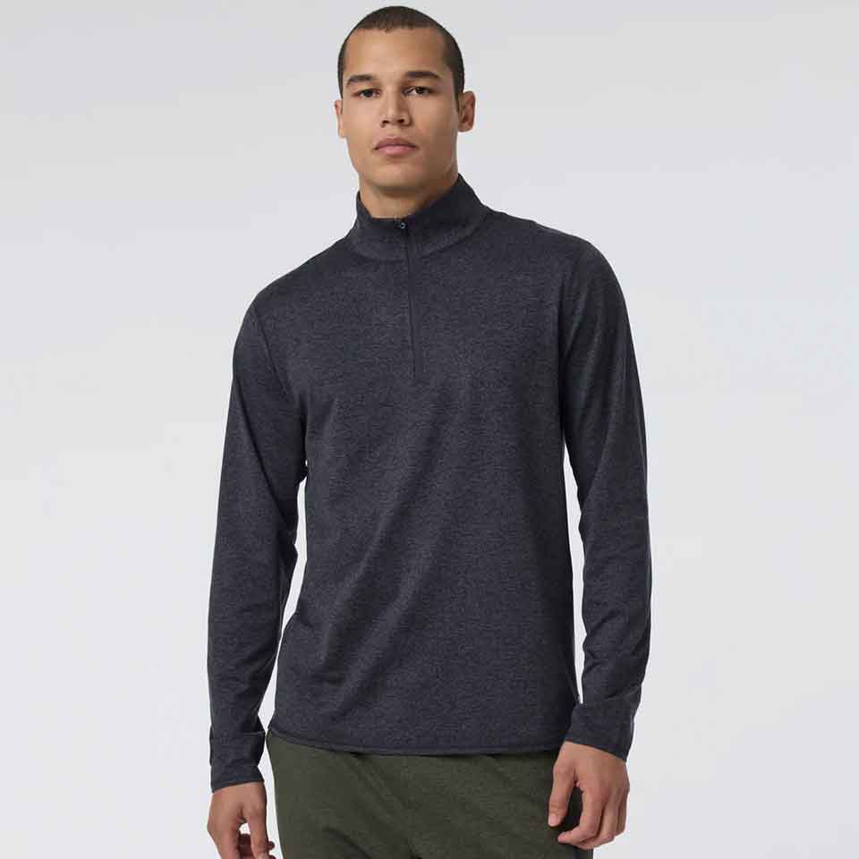A person wearing a Vuori long-sleeve, dark gray quarter-zip pullover and olive green pants stands against a plain, light background—perfect golf apparel for Father’s Day.