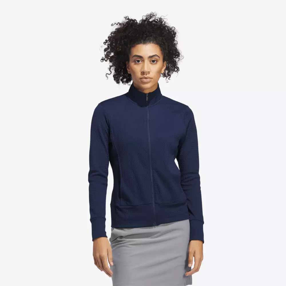 A woman with curly hair is wearing a navy blue zip-up jacket and a light gray skirt, showcasing stylish apparel perfect for Mother’s Day, standing against a plain white background.