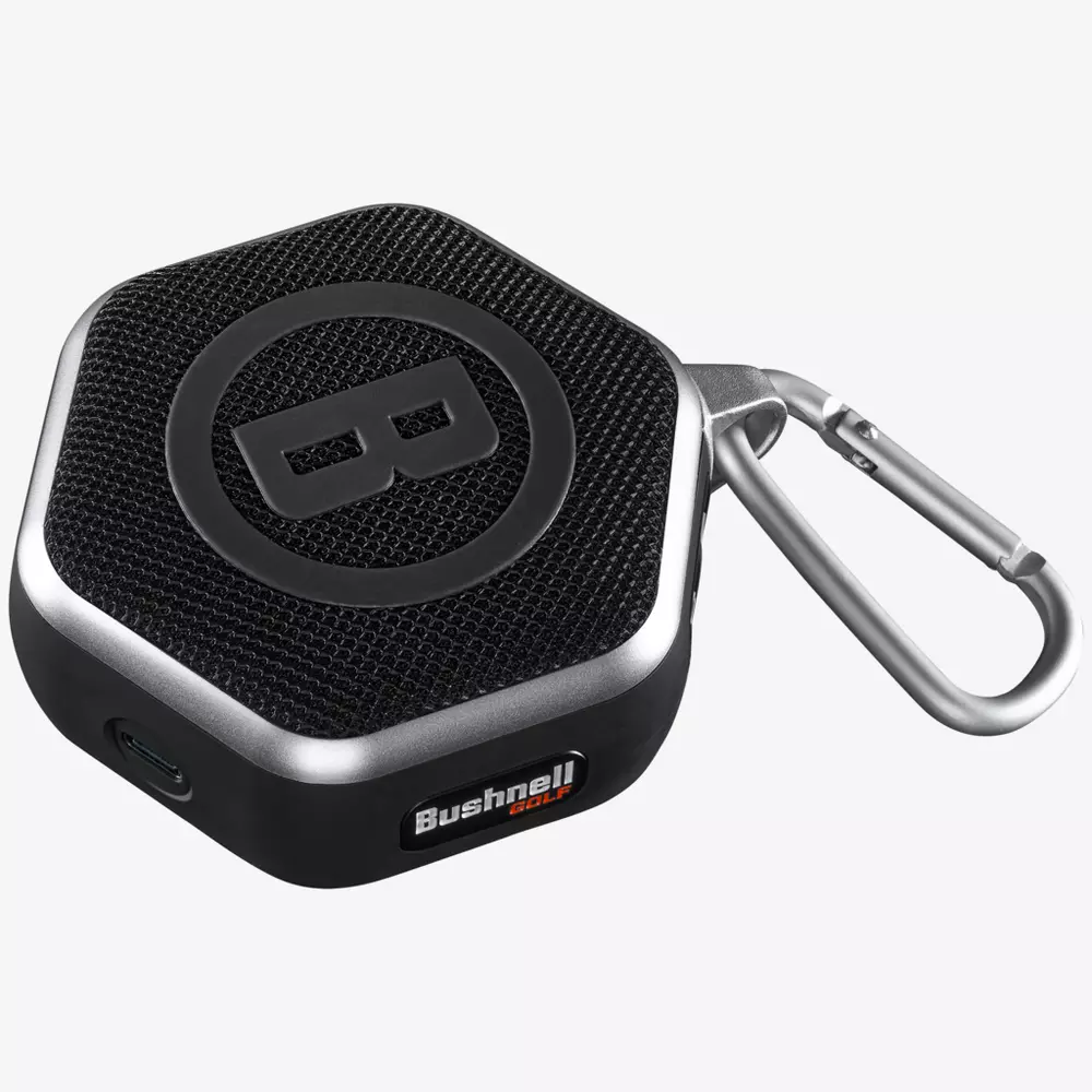A compact, black, hexagonal portable speaker with a textured grille, large B logo on top, attached silver carabiner, and Bushnell branding&mdash;an ideal companion for those seeking the best golf smartwatch experience on the course.
