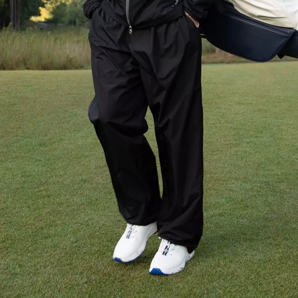 Person standing on grass wearing black pants and a black jacket, with white athletic shoes that have blue soles&mdash;perfect for checking out the 6 Golf Deals Worth Buying Right Now. Their upper body is mostly out of frame.