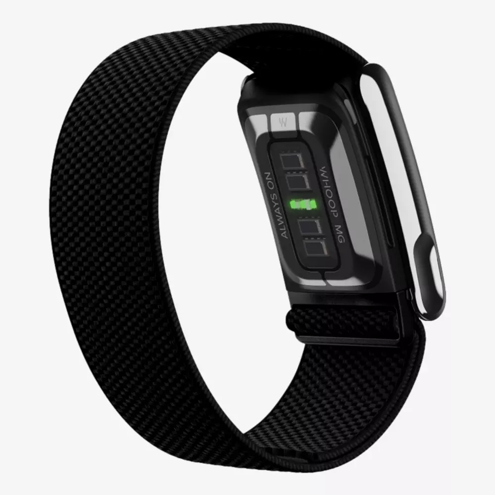 A black fitness tracker with a fabric strap is shown from the back, displaying its heart rate sensor and metallic clasp. The screen indicates text and a green light from the sensor&mdash;proof that summer is the right time to stay active, rain or shine!.