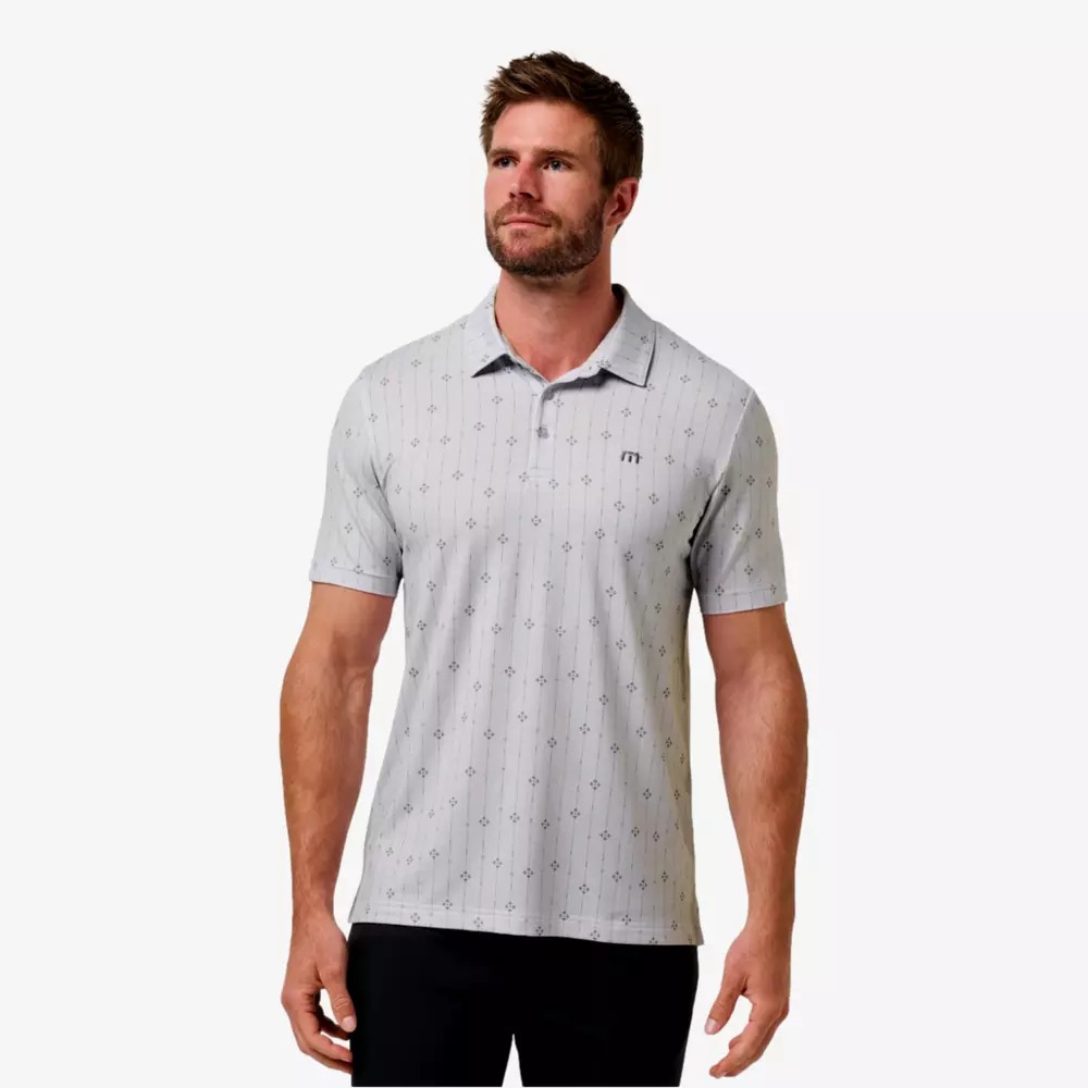 A man with short brown hair and a beard wears a light grey, short-sleeve polo shirt with a subtle dotted pattern and black pants, standing against a plain white background, ready to pair his look with the best golf smartwatch.